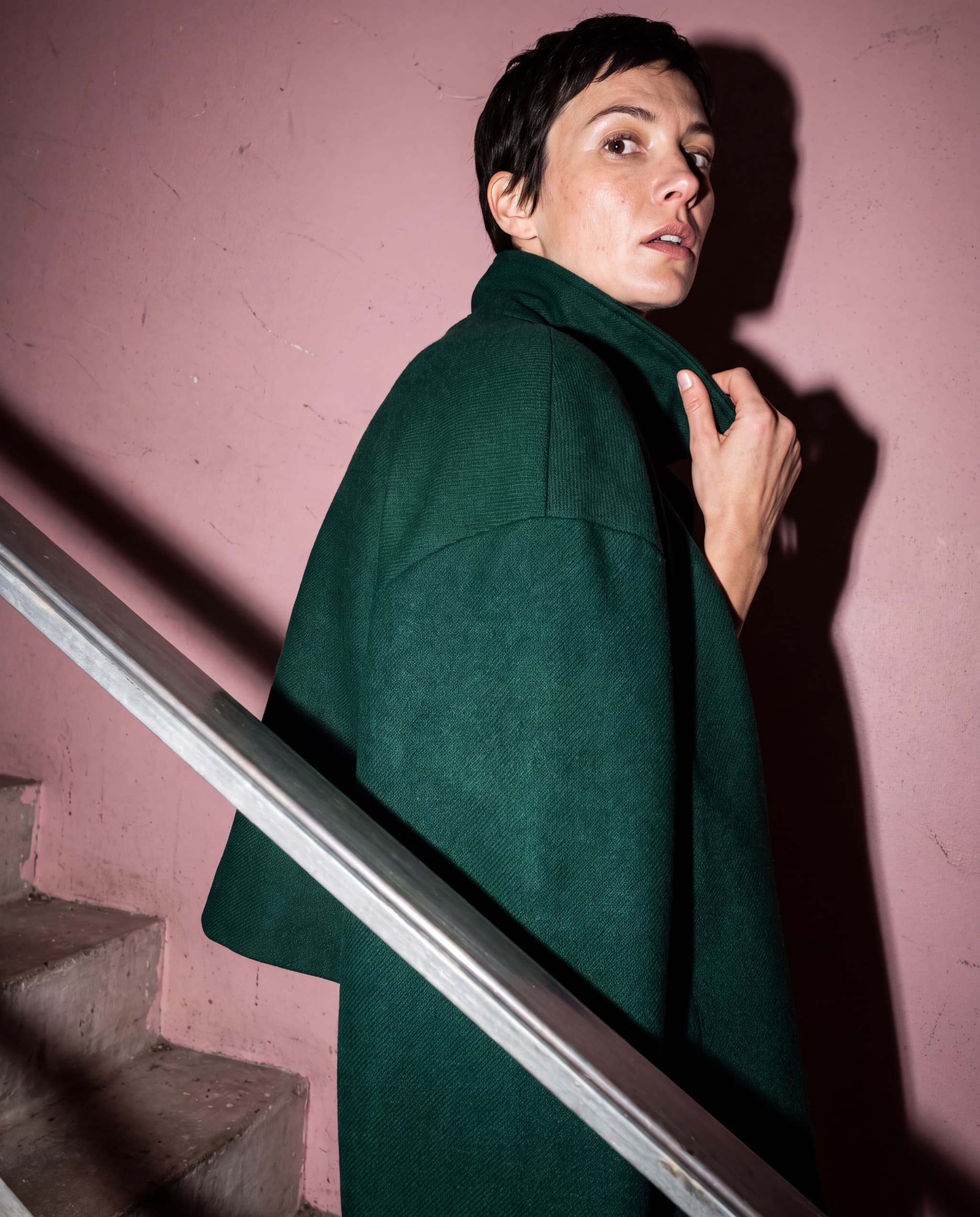 Retrato de moda cercano con una capa verde botella en una escalera rosa empolvado.