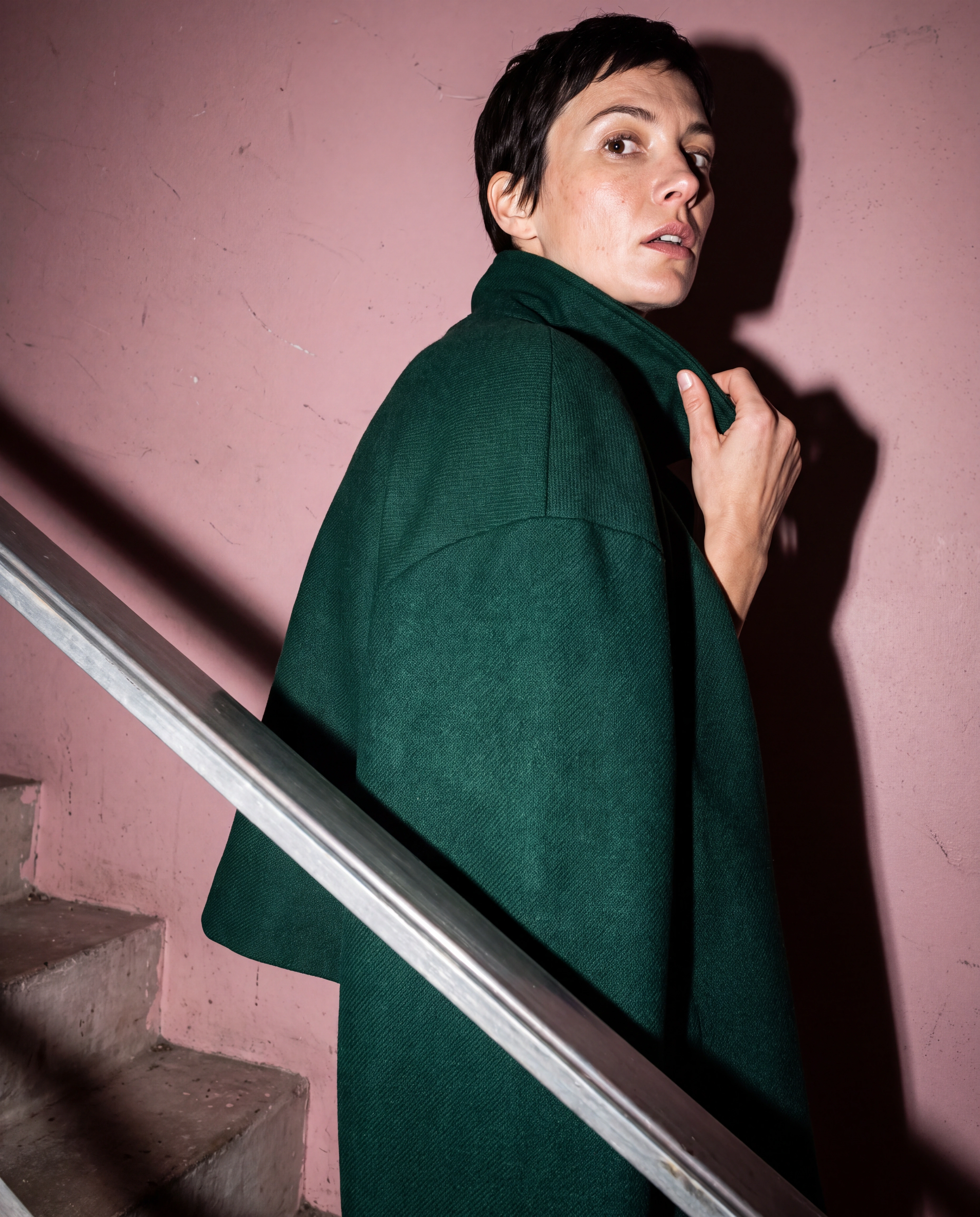 Retrato de moda cercano con una capa verde botella en una escalera rosa empolvado.
